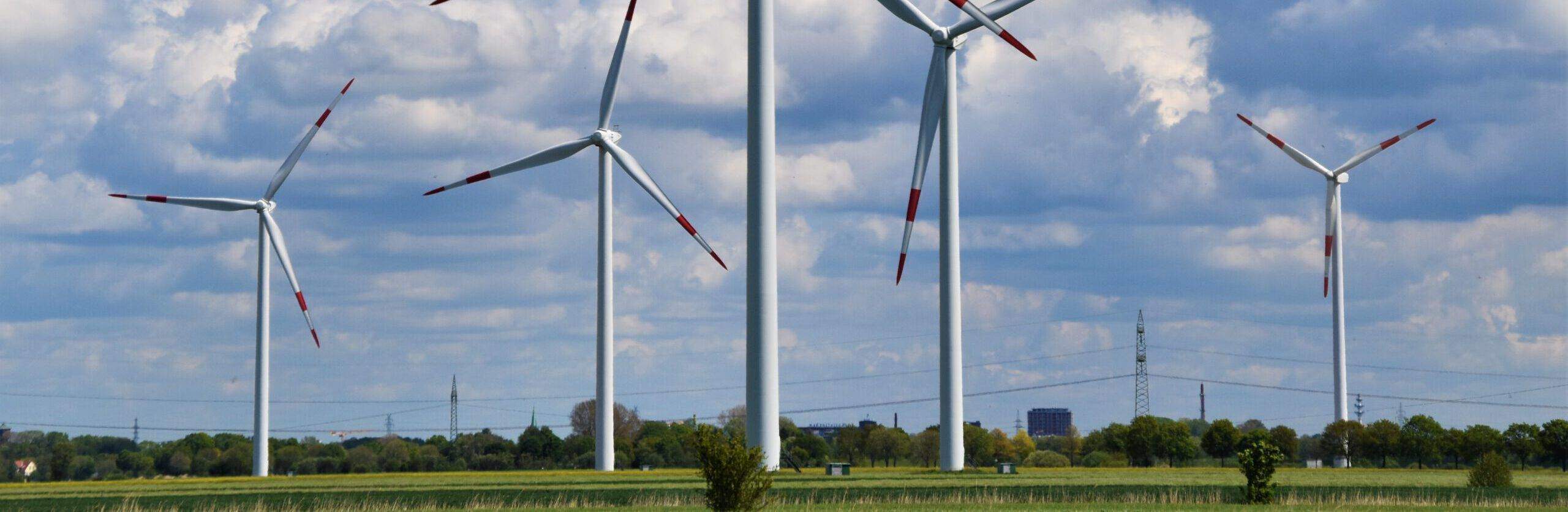 Mehrere Windkraftanlagen stehen in einem Windpark auf einem Feld und erzeugen erneuerbare Energien