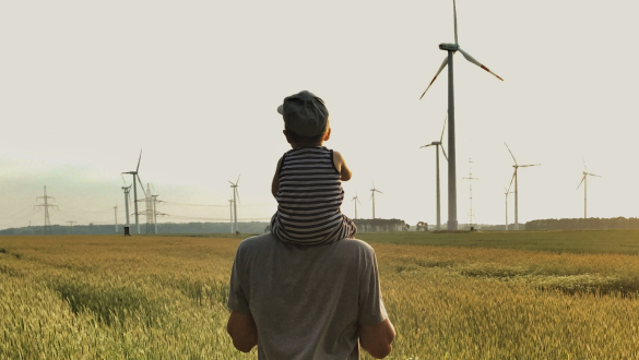 Ein Mann hat sein Kind auf den Schultern und steht vor einem Feld mit vielen Windrädern für Nachhaltige Energie