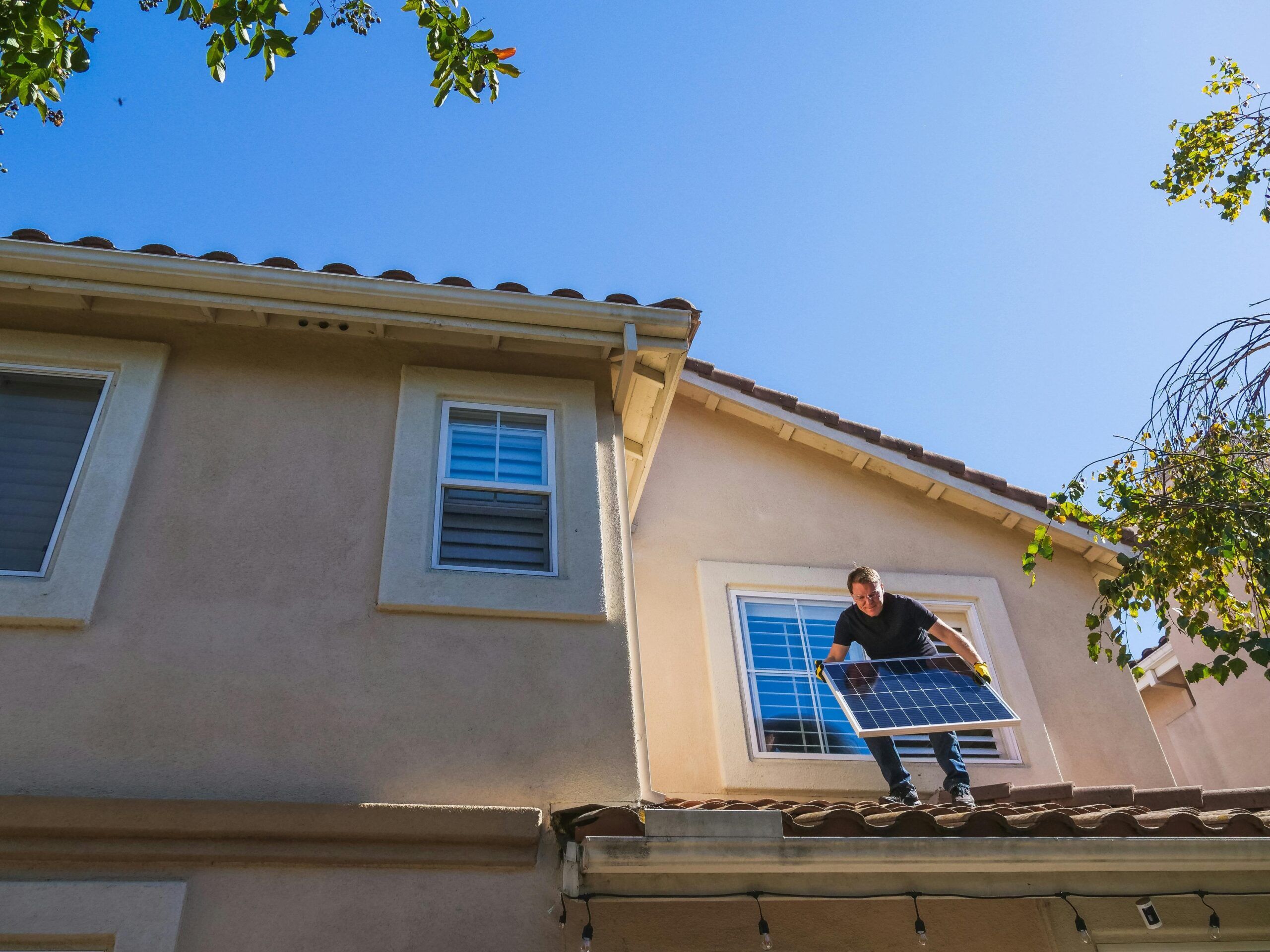 Ein Mann steht auf dem Dach mit einer Photovoltaikplatte und sorgt für bessere Energieversorgung